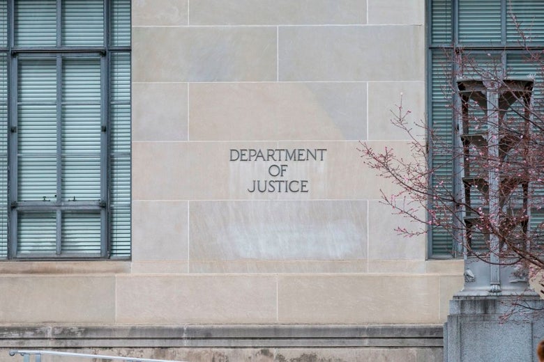 A brick wall between large windows with the words "Department of Justice" etched into it.